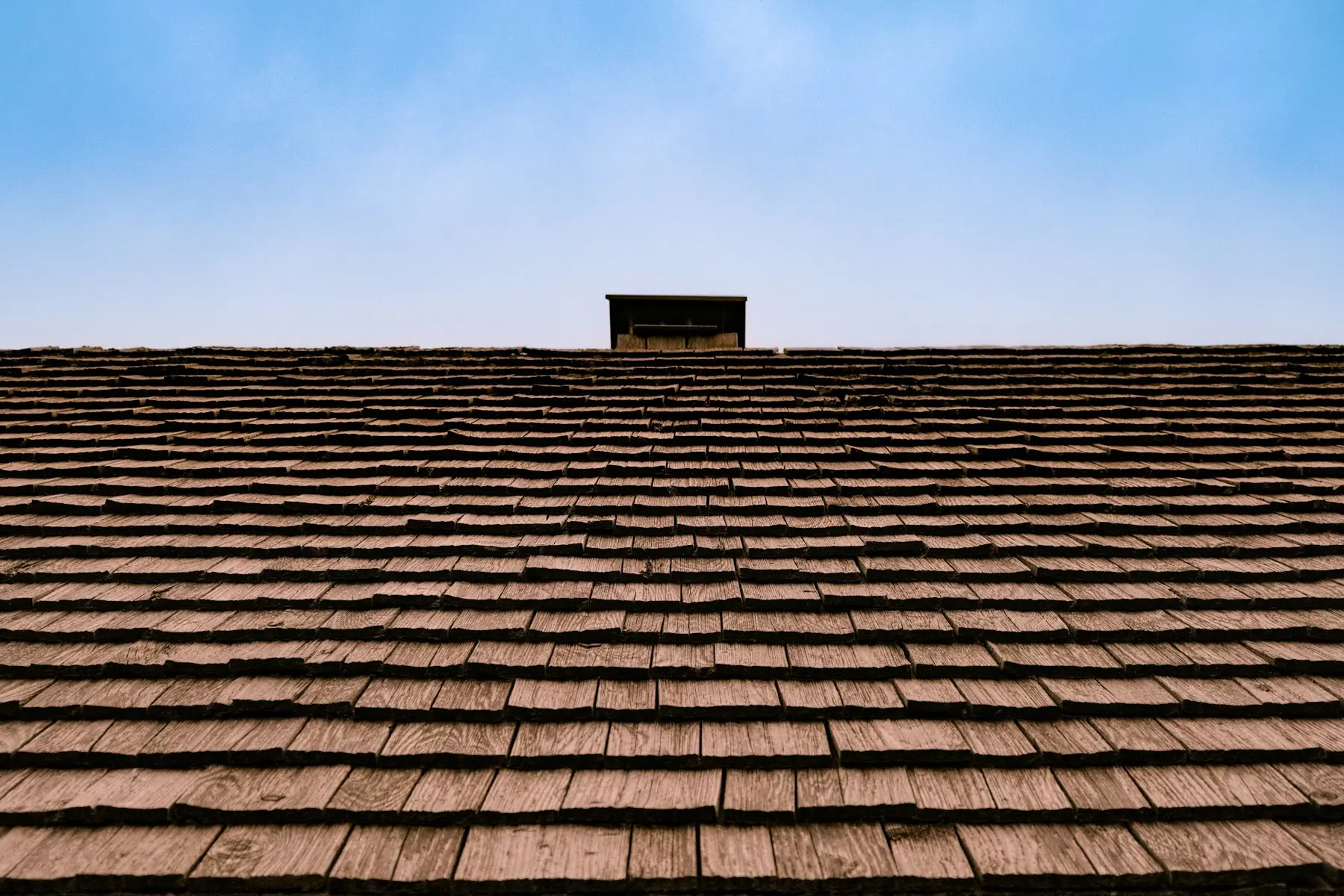 Rows of weathered brown shingles meeting a pale blue sky