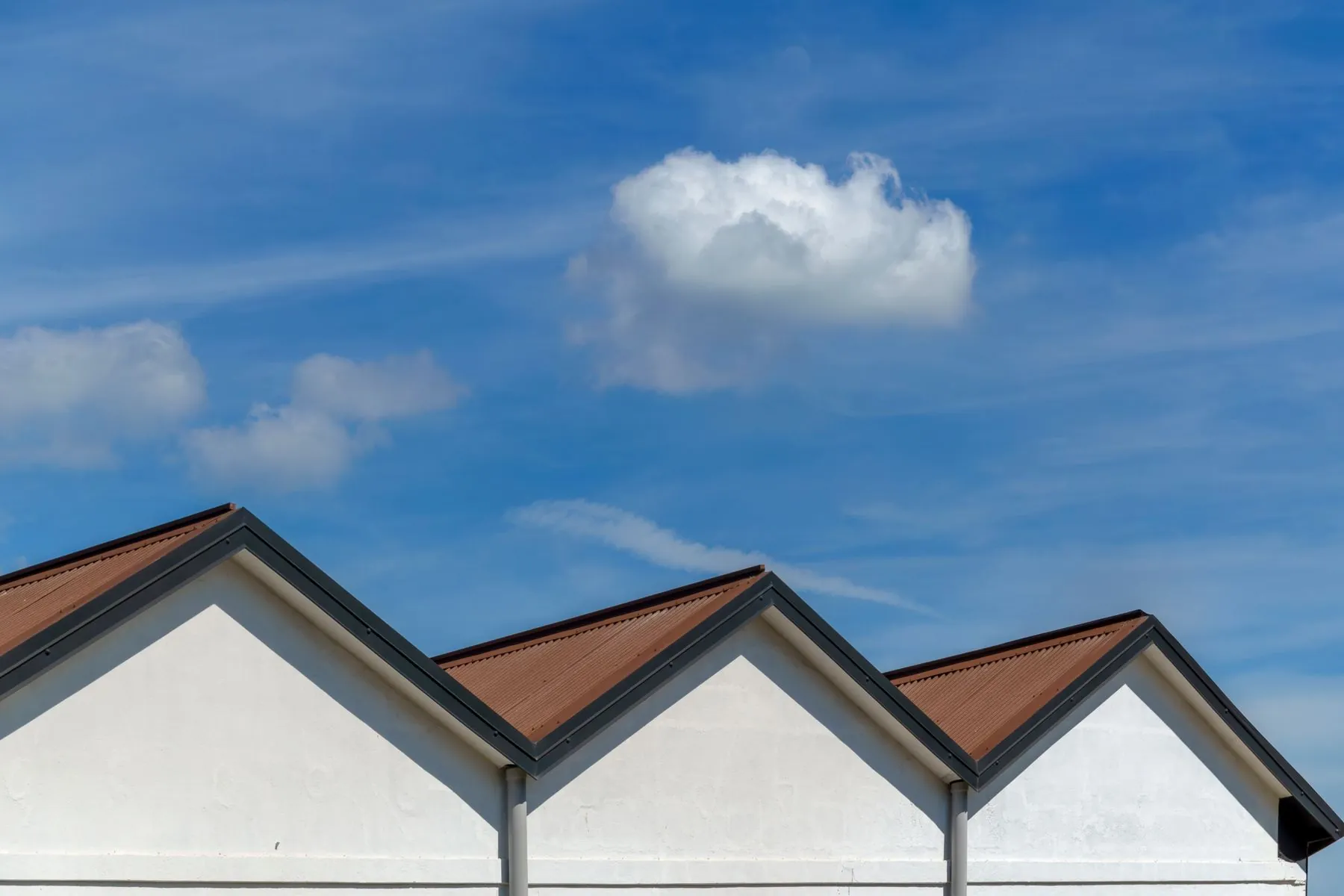 Three sharp roof gables with copper-brown shingles against a blue sky with clouds
