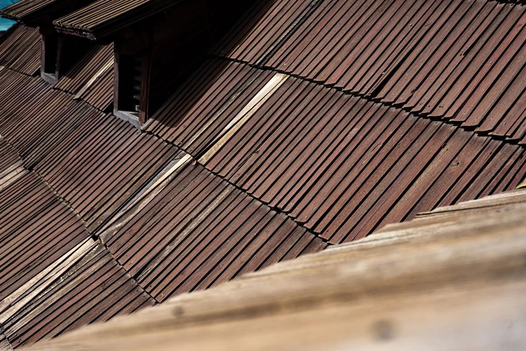 Aged dark brown wooden roof shingles at an angle with a dormer